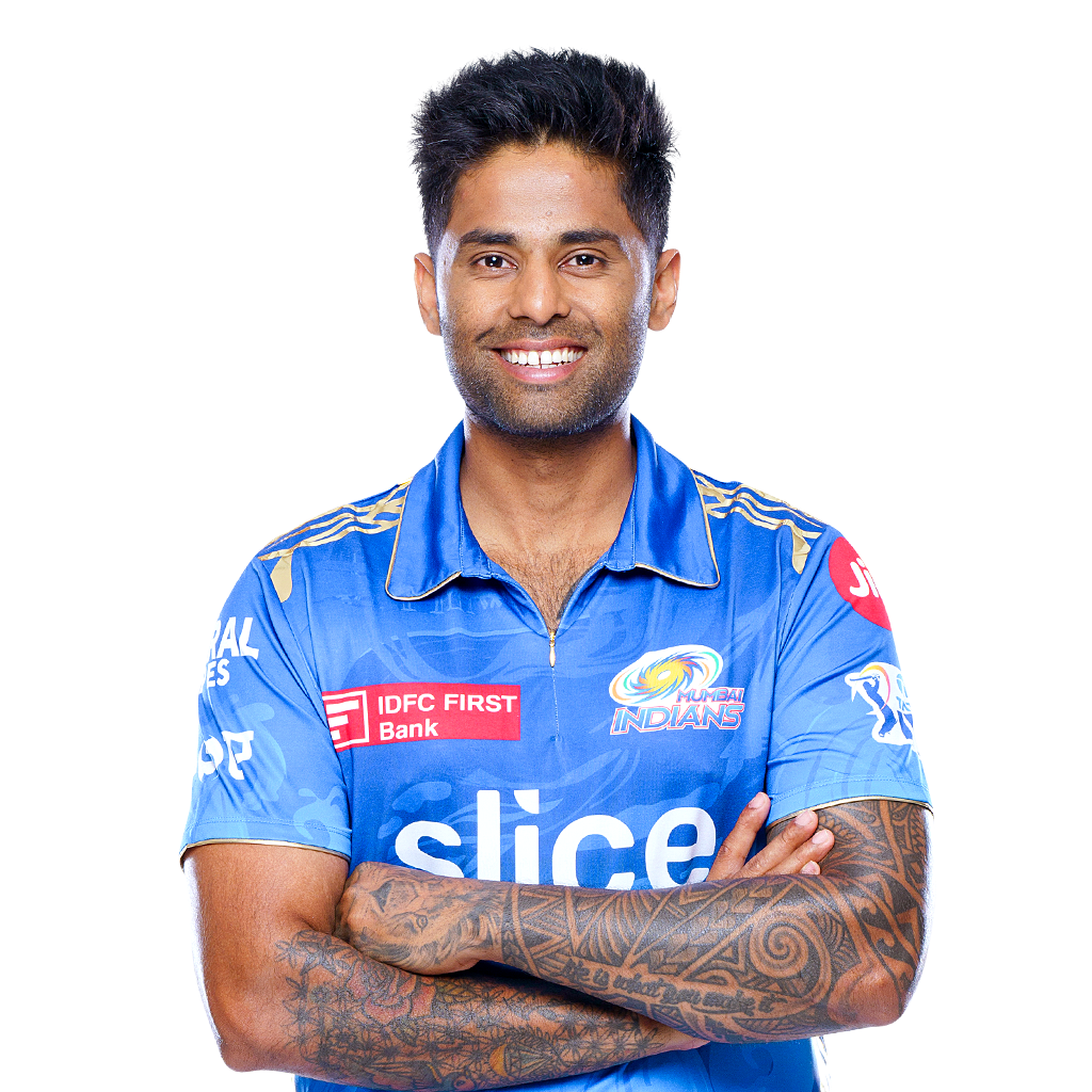 Smiling cricket player in a blue Mumbai Indians jersey with tattooed arms crossed.