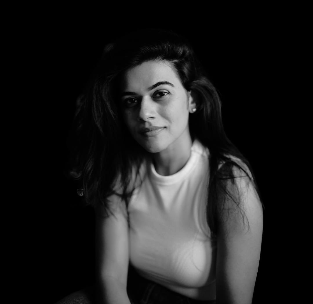 Black-and-white portrait of a woman with long hair wearing a sleeveless top against a dark background.
