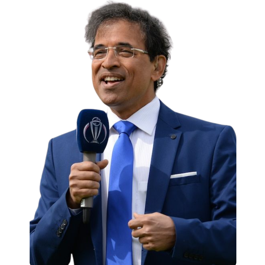 Man wearing a blue suit, white shirt, and blue tie holding a microphone with a cricket trophy logo, smiling and speaking.