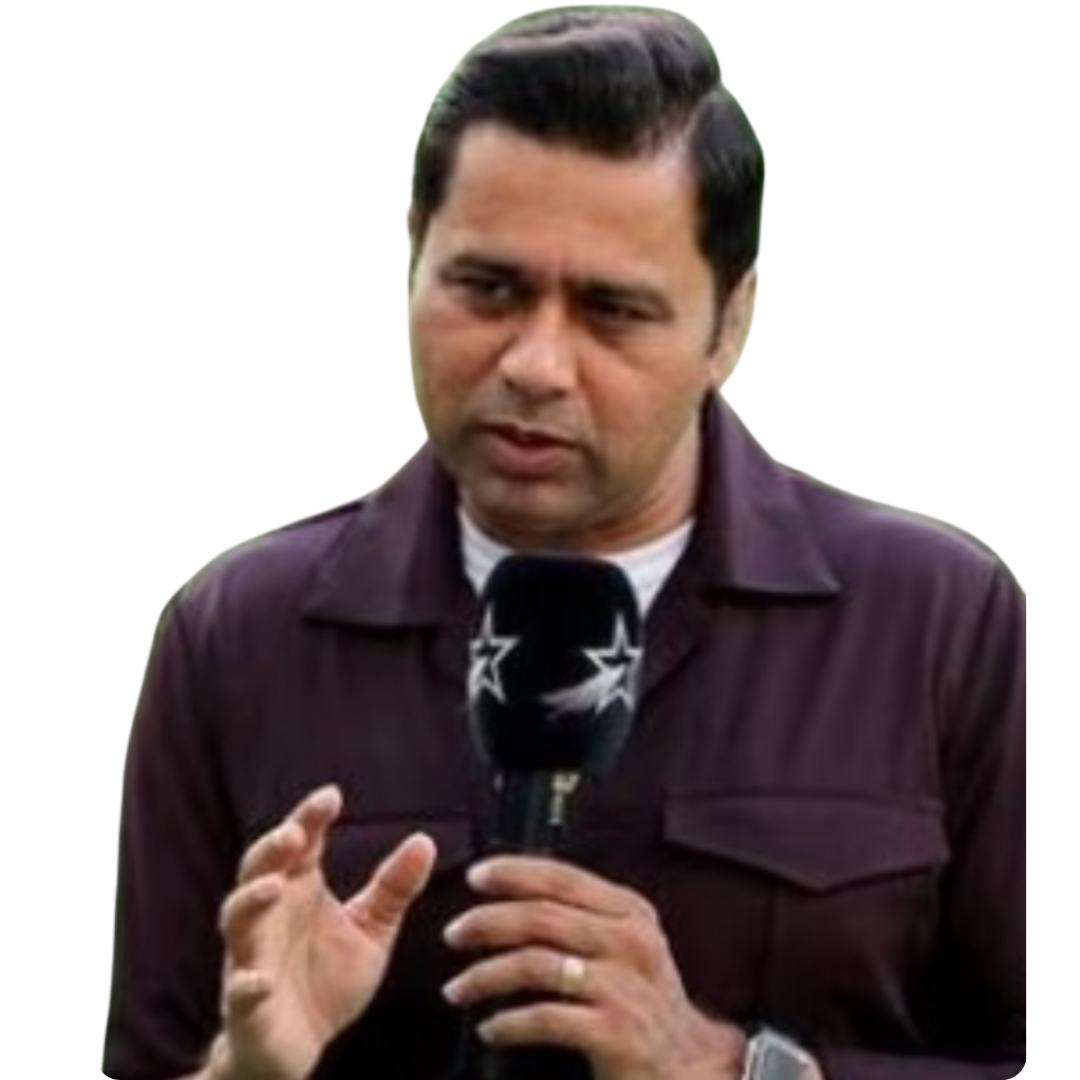 Man with short dark hair speaking into a microphone with star logos, wearing a dark purple shirt and a wristwatch, gesturing with his left hand.