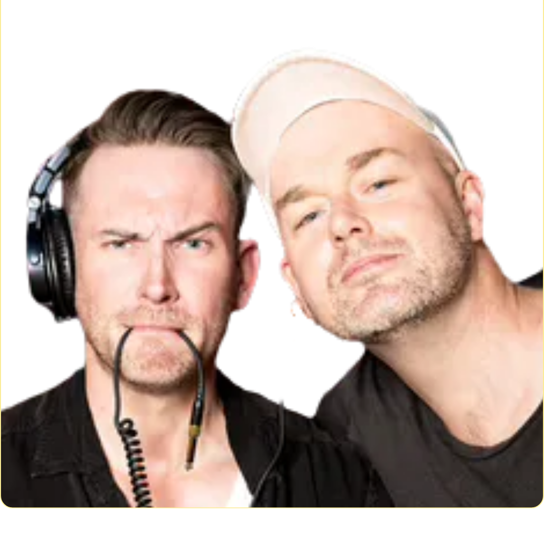 Two men close together against a black background; the man on the left wears headphones and holds an audio cable in his mouth with a puzzled expression, the man on the right wears a white cap and a slight smile.