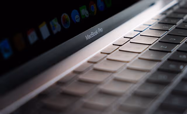 Close-up view of a MacBook Pro keyboard with the screen partly visible showing app icons.