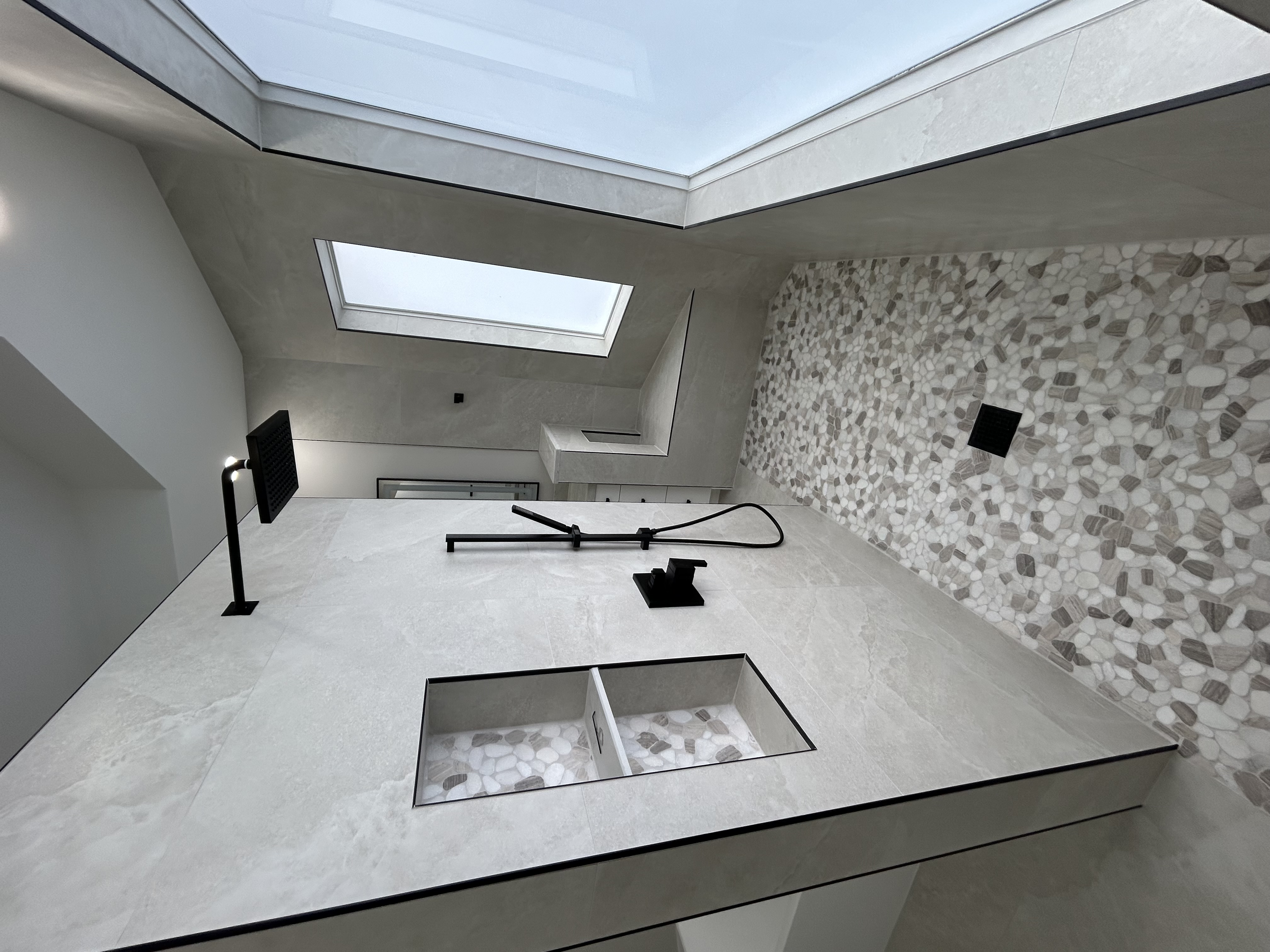 Modern bathroom with double sinks, large mirror, white countertop, glass-enclosed shower, toilet, and dark gray towels and rugs.