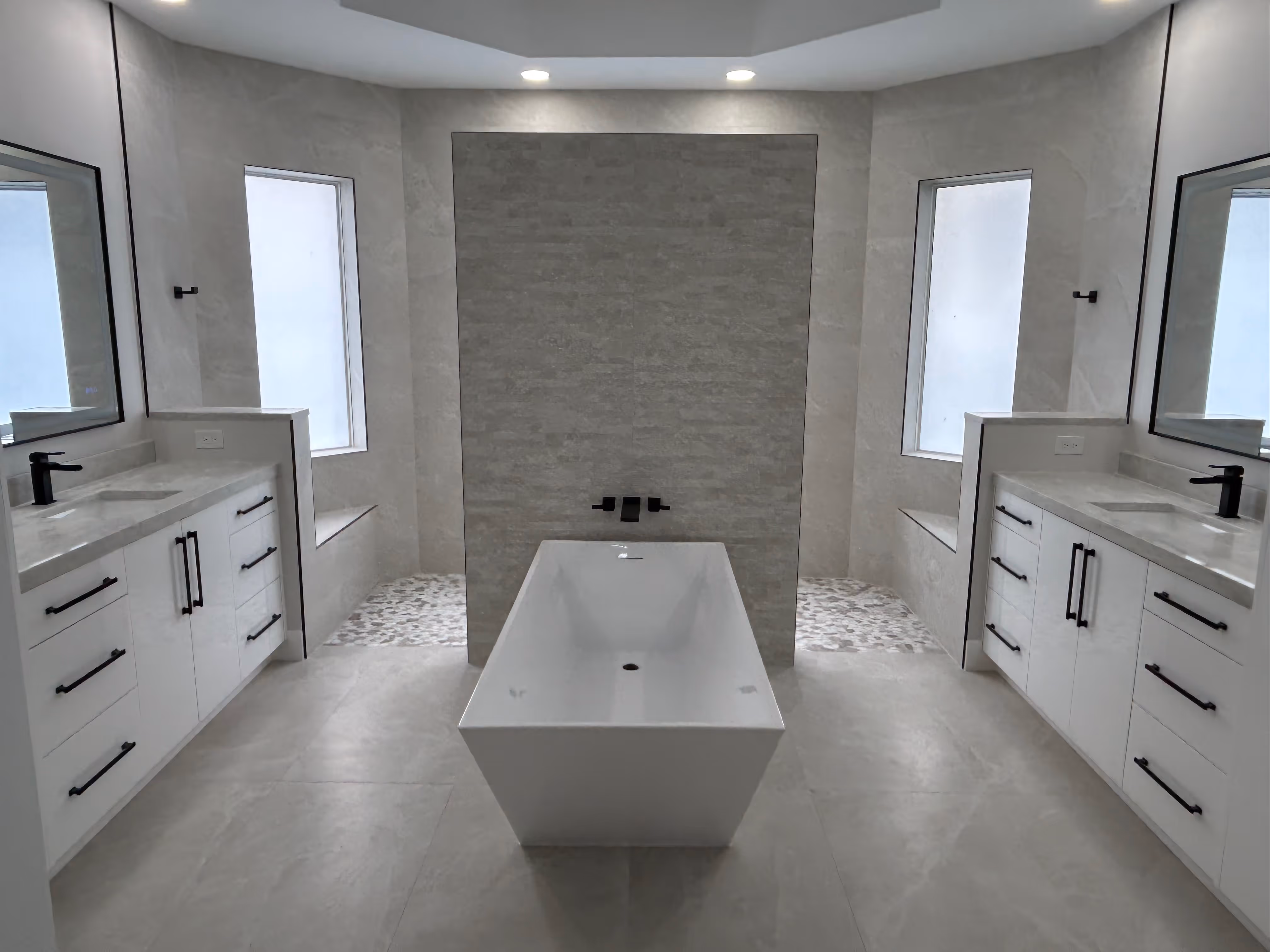 Modern bathroom with a central freestanding bathtub, two vanities with black faucets and handles, large mirrors, and frosted windows.