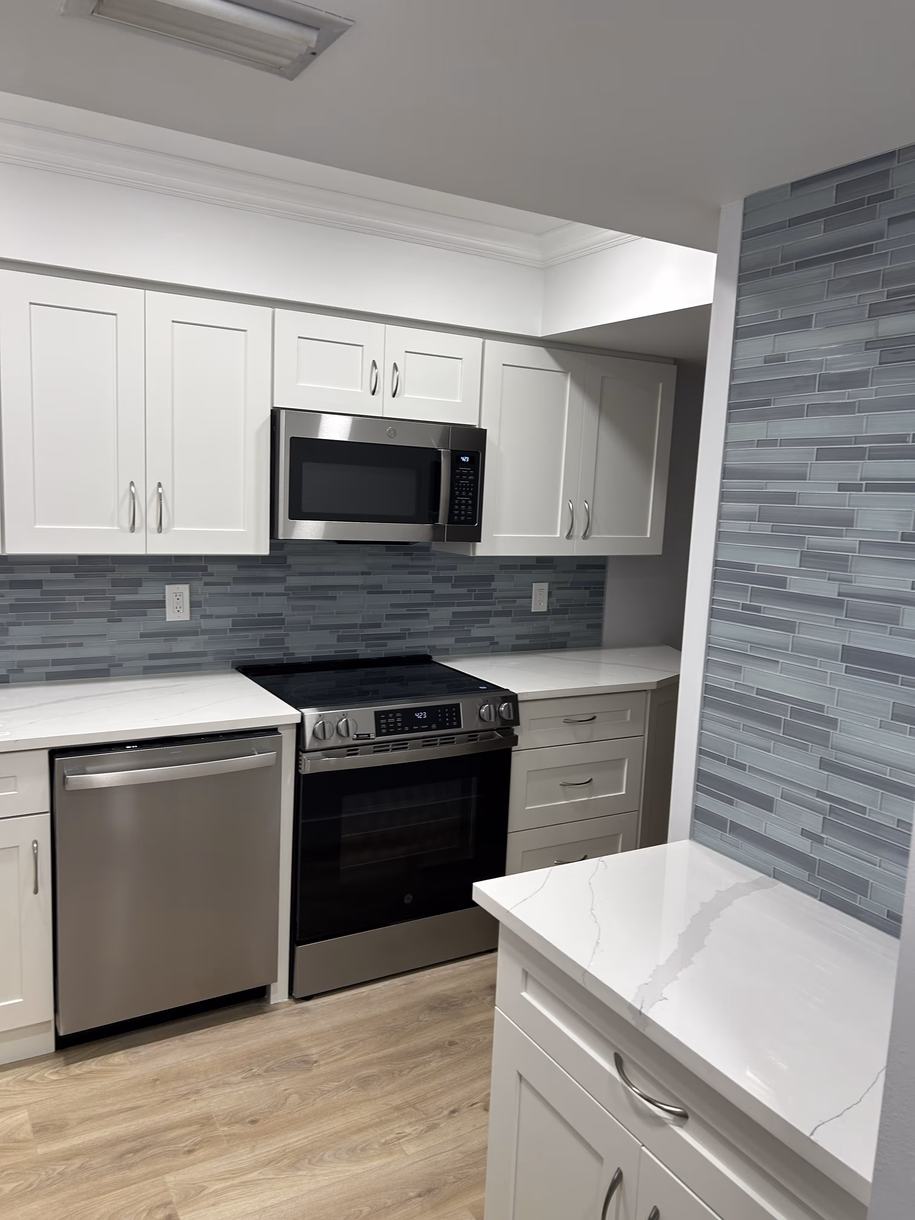 Modern kitchen with white cabinets, stainless steel appliances, blue tile backsplash, and light wood floor.