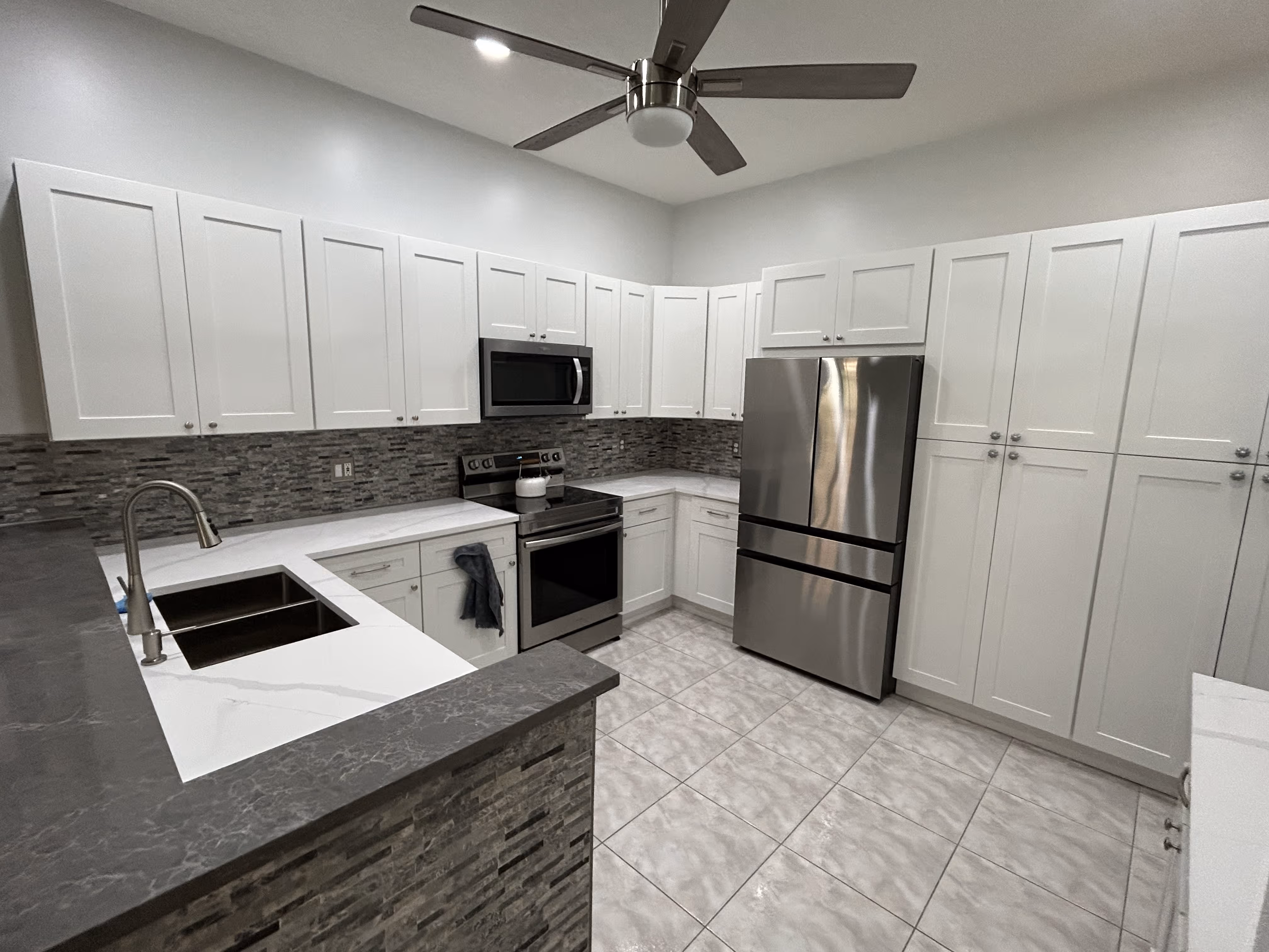 Modern kitchen with white cabinets, stainless steel fridge and stove, gray backsplash, and marble countertops.