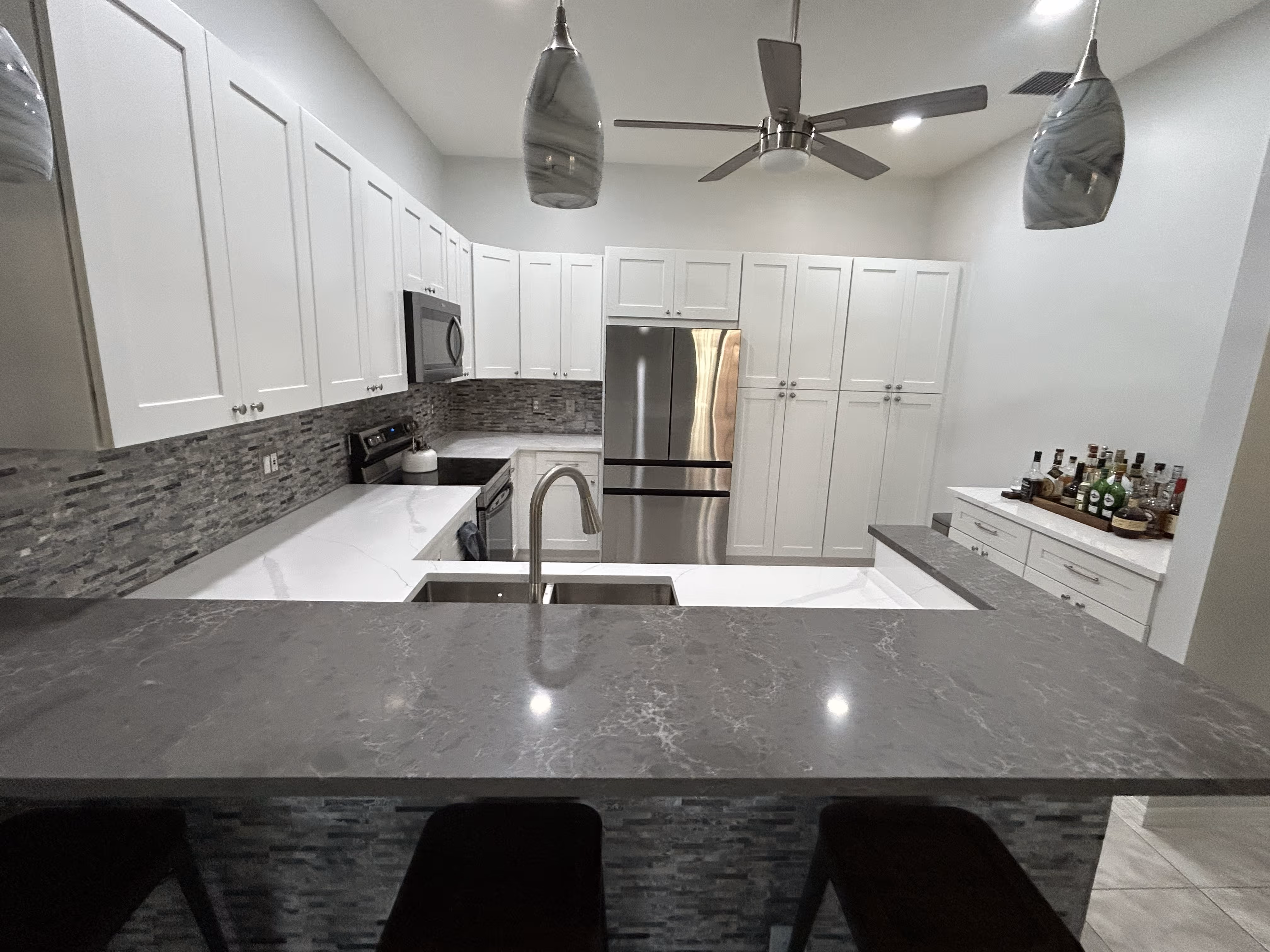Modern kitchen with white cabinets, gray backsplash, stainless steel appliances, and marble countertops.