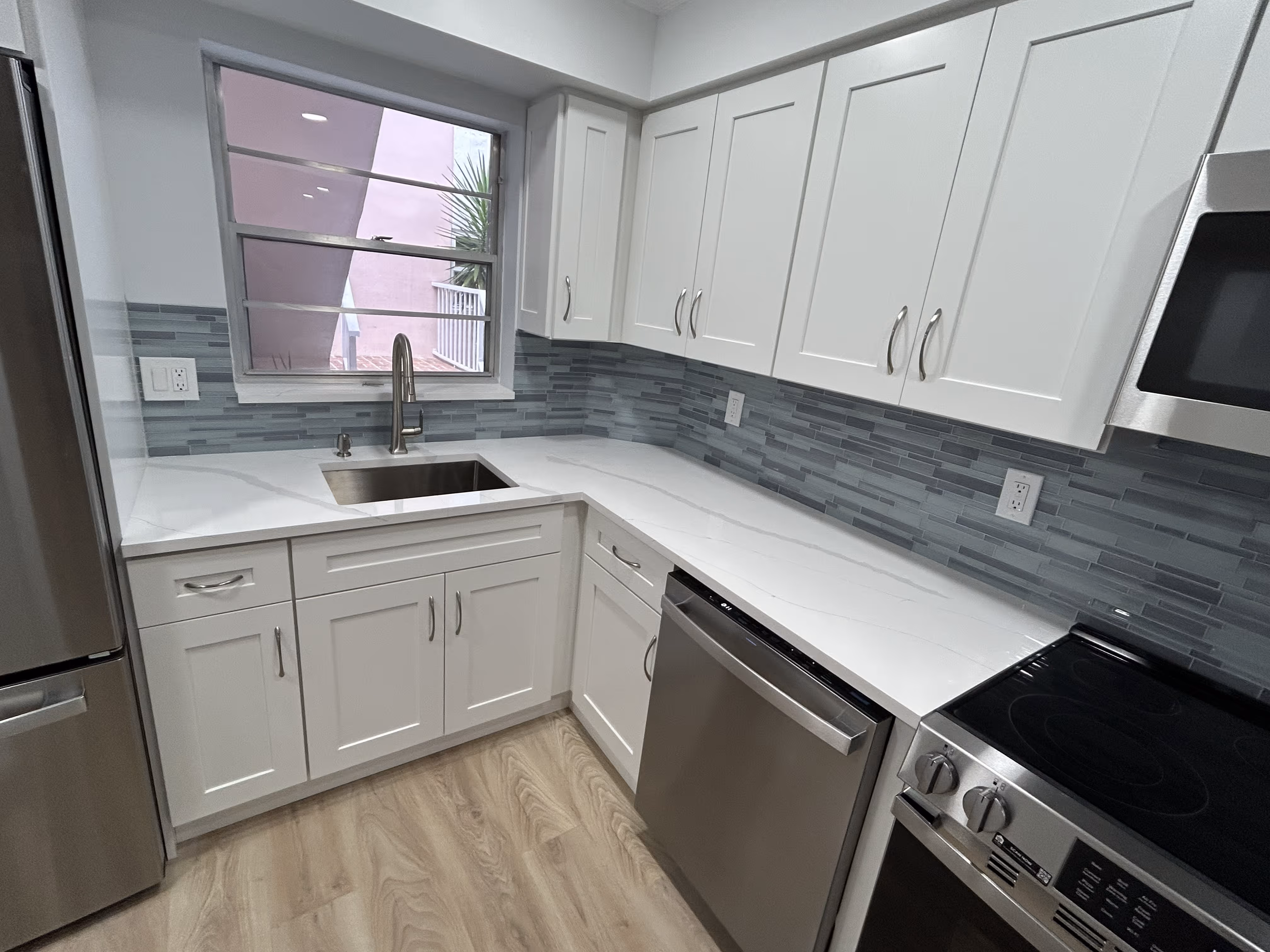 Modern kitchen with white cabinets, gray tile backsplash, stainless steel appliances, and wood flooring.