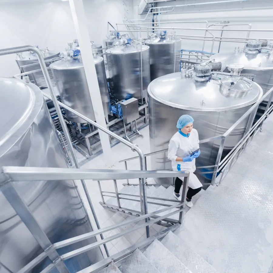worker in a clean, modern industrial facility with large stainless steel tanks.