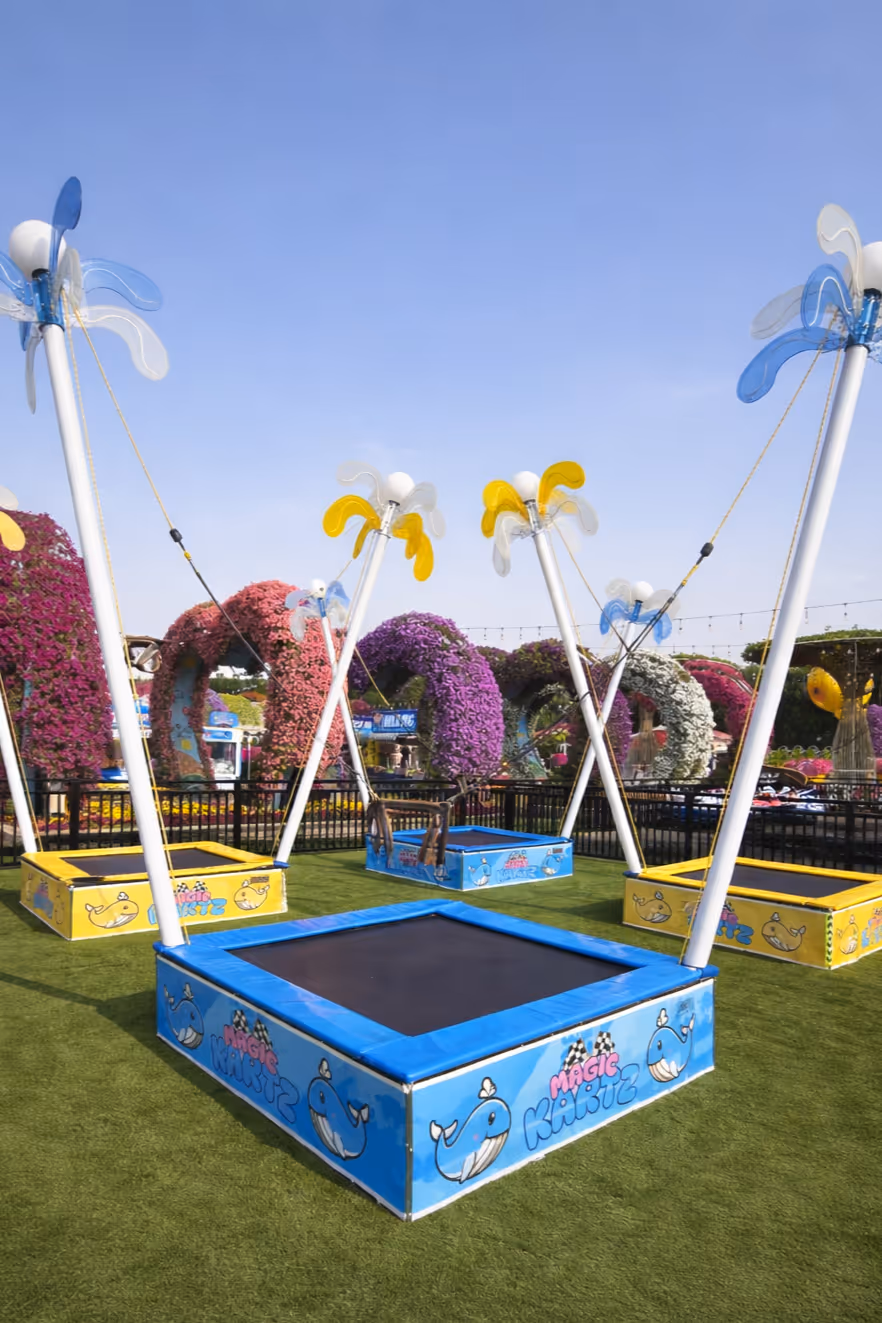 Colorful outdoor trampolines with springy flower decorations on artificial grass in a garden with vibrant flower arches in the background.