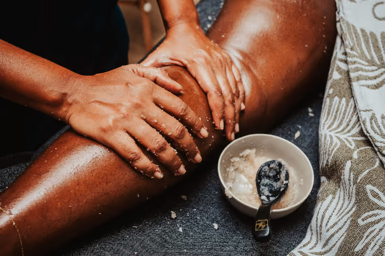 Hands applying salt scrub to leg during an exfoliating body treatment