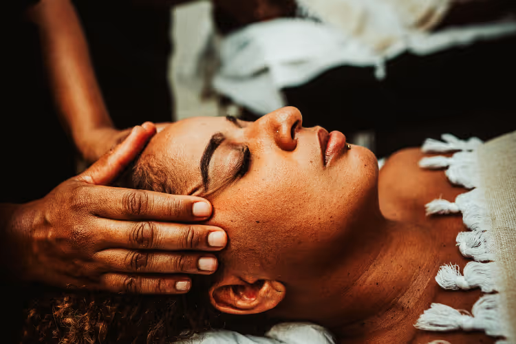 Mains pratiquant un massage facial relaxant sur table de soin drapée de blanc