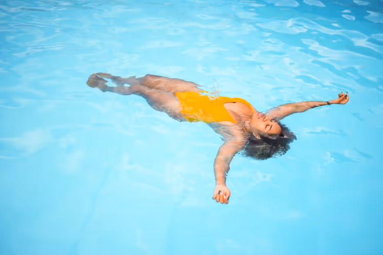 Personne flottant détendue en maillot orange dans piscine eau turquoise