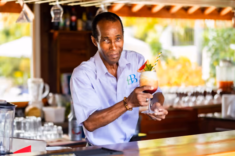 Barman en chemise lilas préparant un cocktail tropical coloré au comptoir du bar
