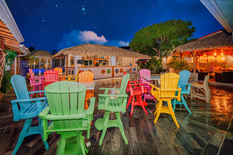Chaises Adirondack multicolores sur terrasse bar tropical toit paillote sous ciel étoilé