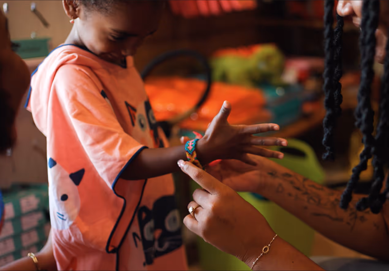Enfant portant t-shirt orange recevant un bracelet tressé coloré