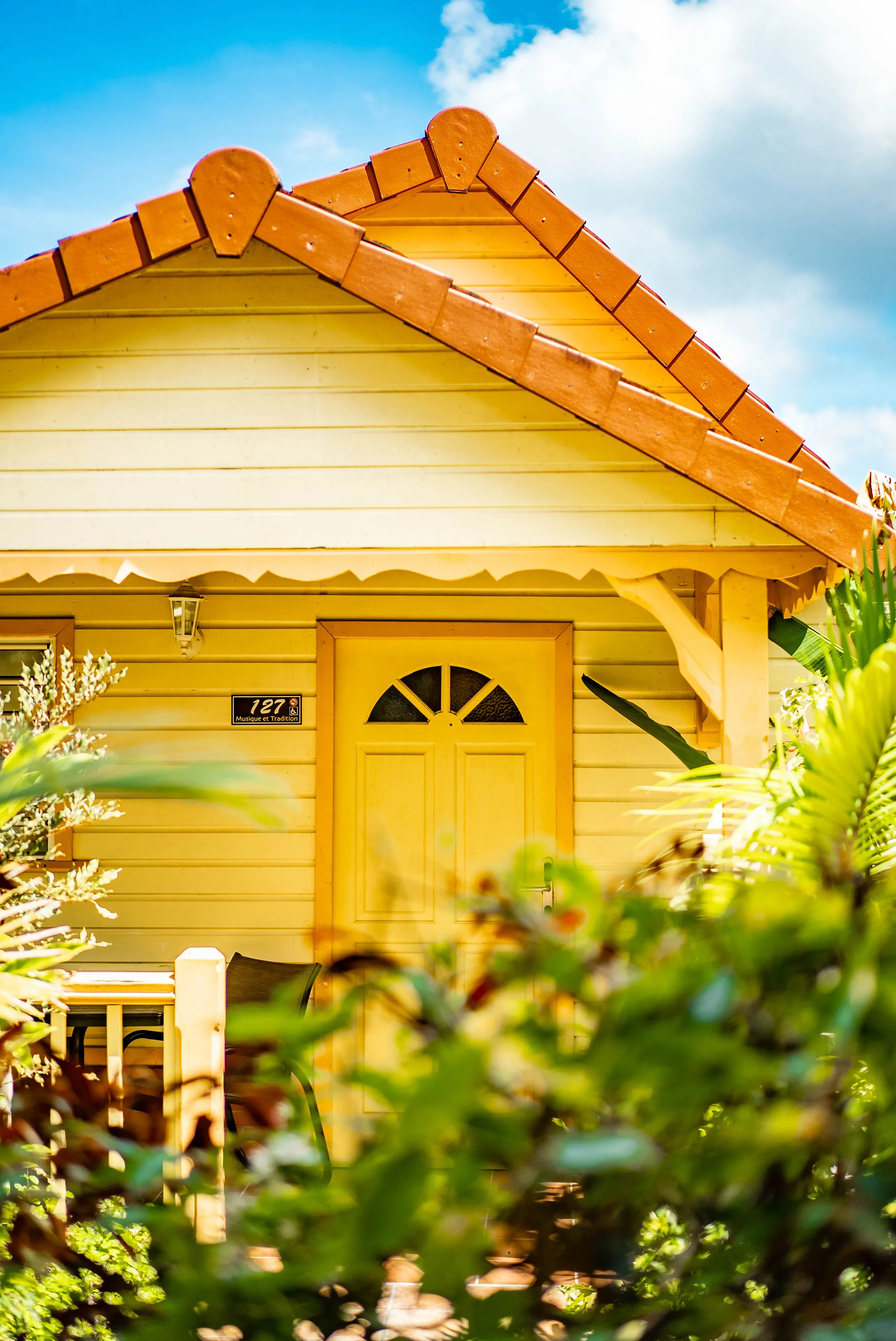 Maison jaune traditionnelle numéro 727 avec toit orange et porte vitrée entourée de végétation tropicale