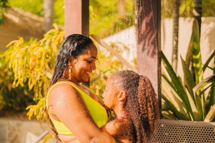 Parent et enfant partagent un moment joyeux sous une douche extérieure dans un jardin tropical ensoleillé