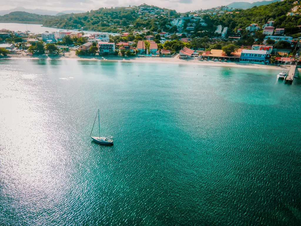 Single-handed sailing yacht on turquoise waters Martinique bay aerial view mountain resort