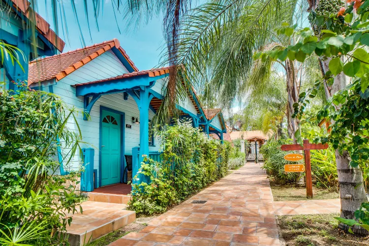 Turquoise-blue tropical bungalow lined with palm trees on paved driveway Bambouresort Martinique