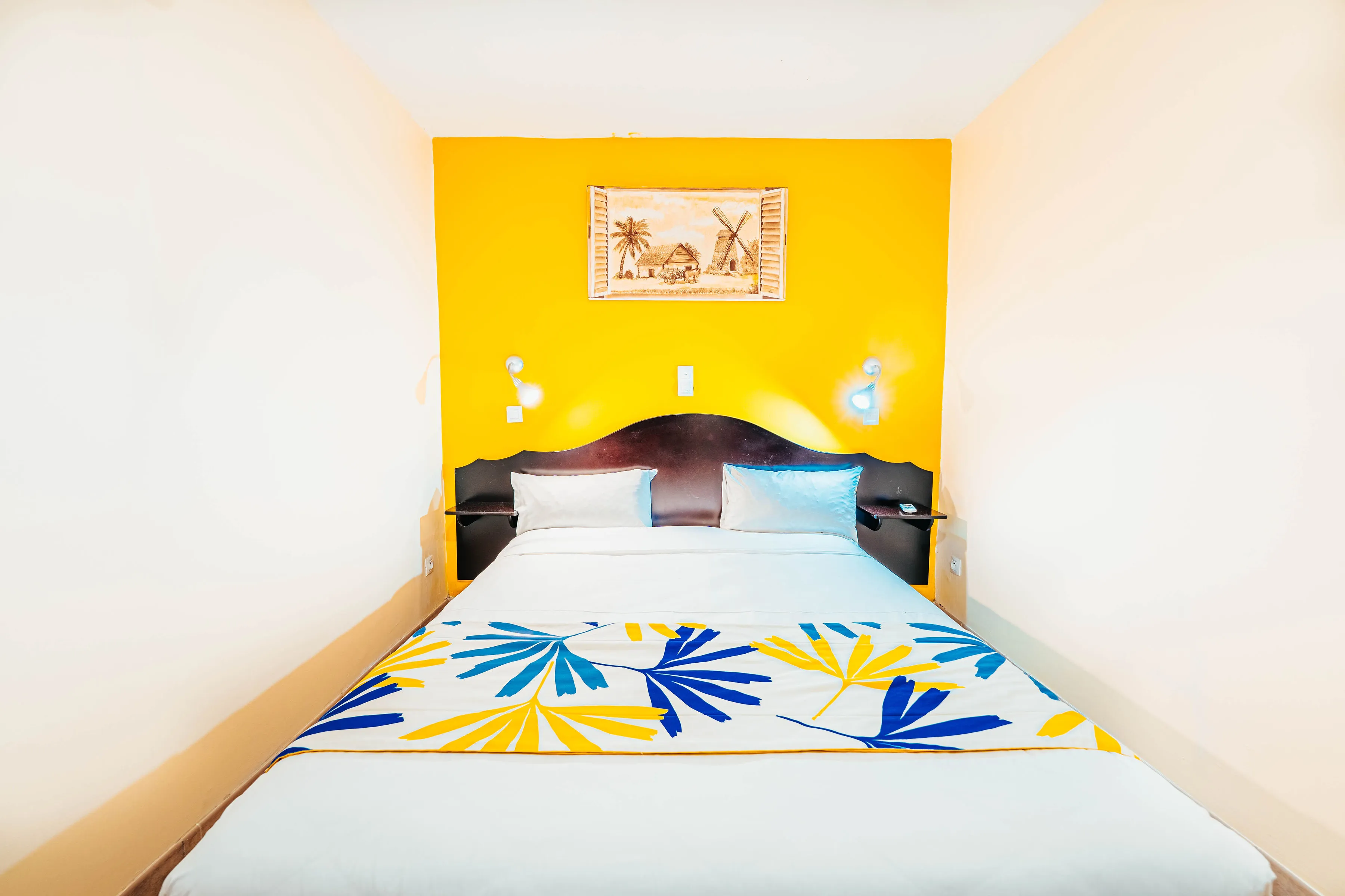 Double bed with tropical bedspread with blue and yellow flower motif on Martinique sun wall