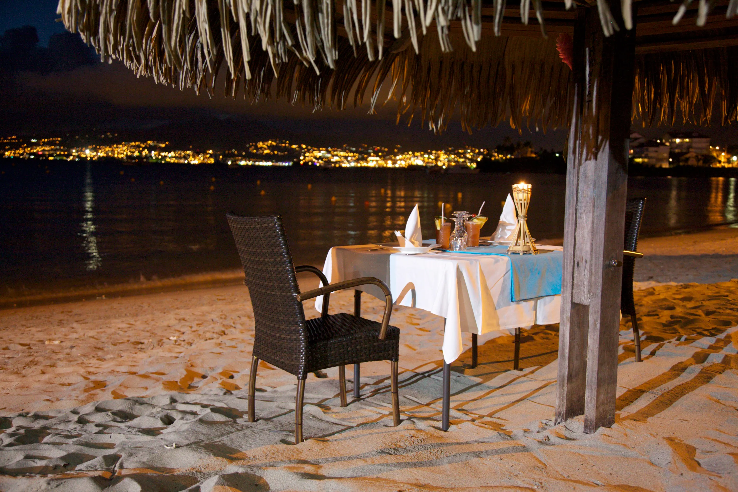 Romantic table under a straw hut on the beach Martinique night view illuminated city