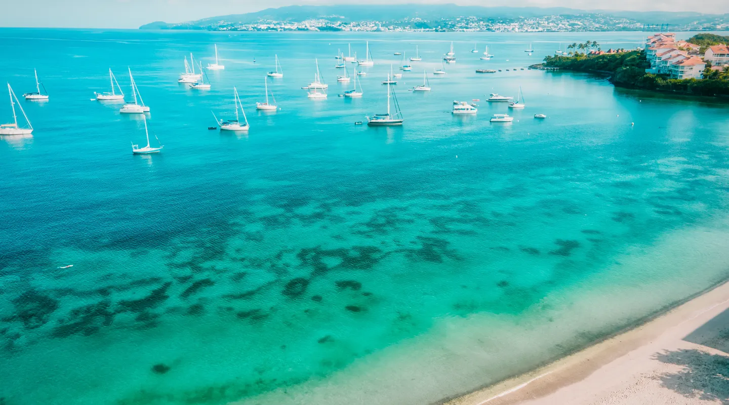 Sailboats anchored in turquoise lagoon bordering Martinique beach aerial view BambouResort