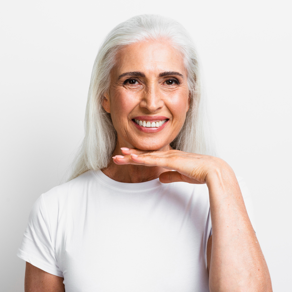 Smiling older woman with long white hair resting her chin on her hand against a white background.