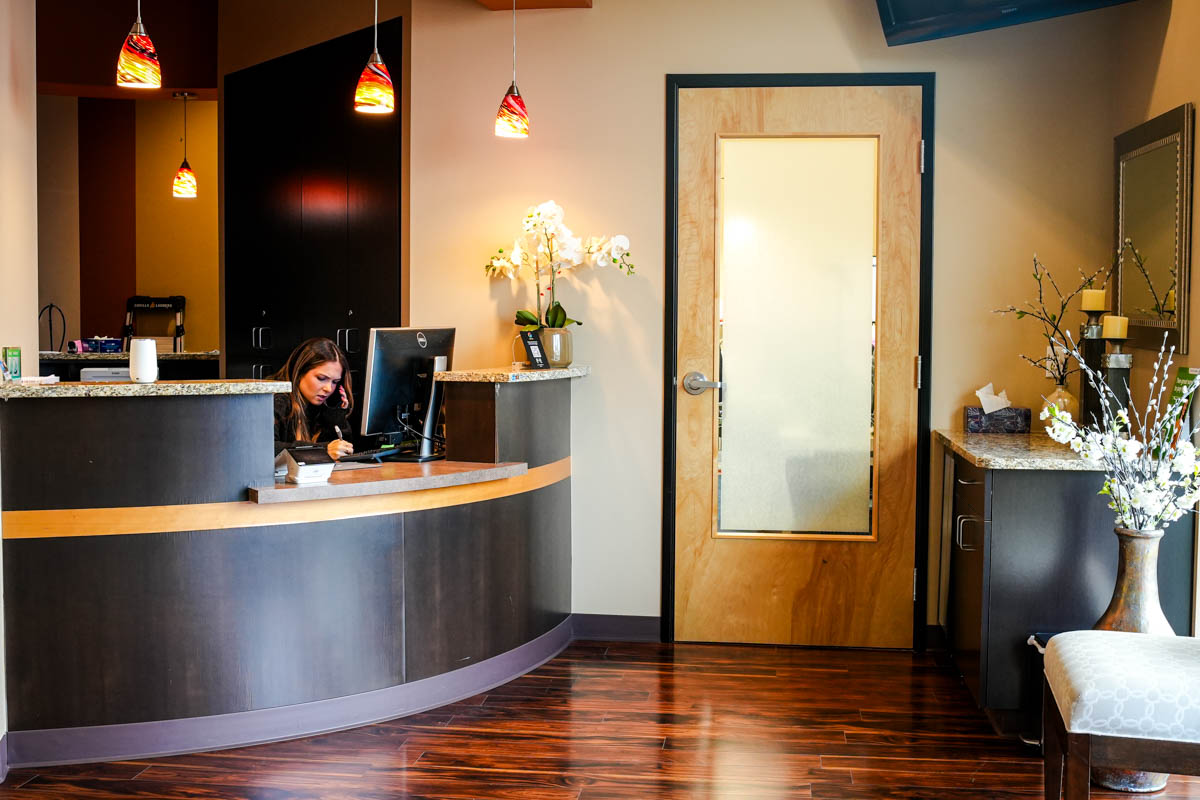 Reception area with a woman working at a dark curved desk, wooden floor, and a door with frosted glass panel.