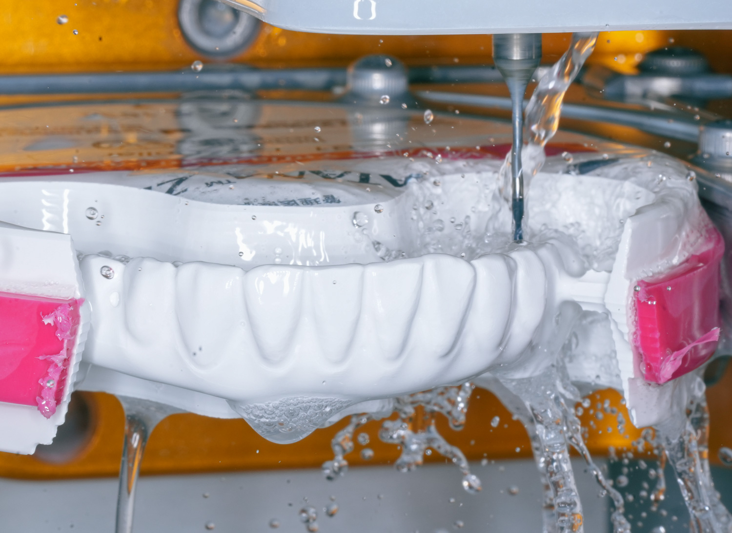 Close-up of a dental mold being machined with water cooling spray and a drill.