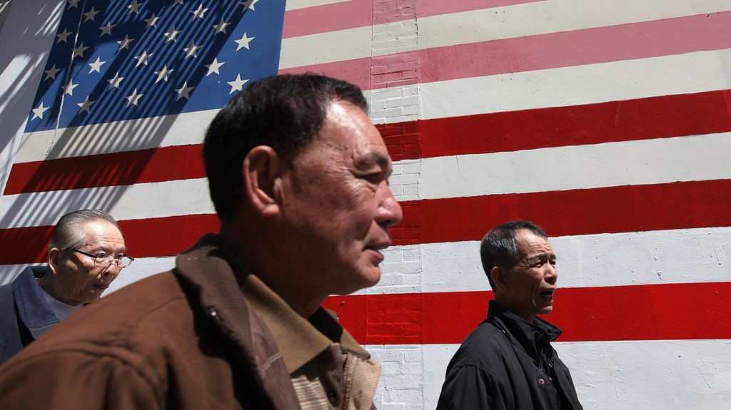 elderly asian american next to a wall of usa flag