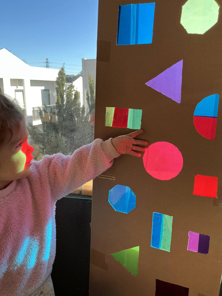 A child exploring coloured light through cellophane shapes at a sunny window