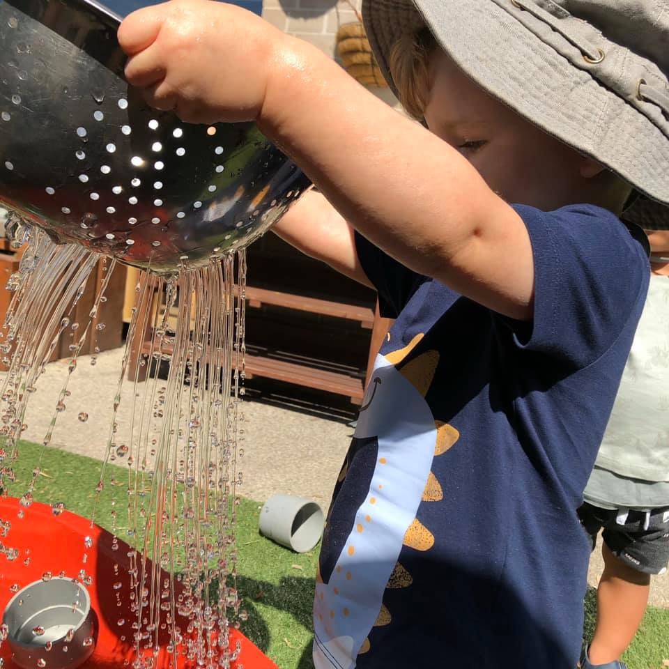 A child pouring water through a colander during outdoor water play