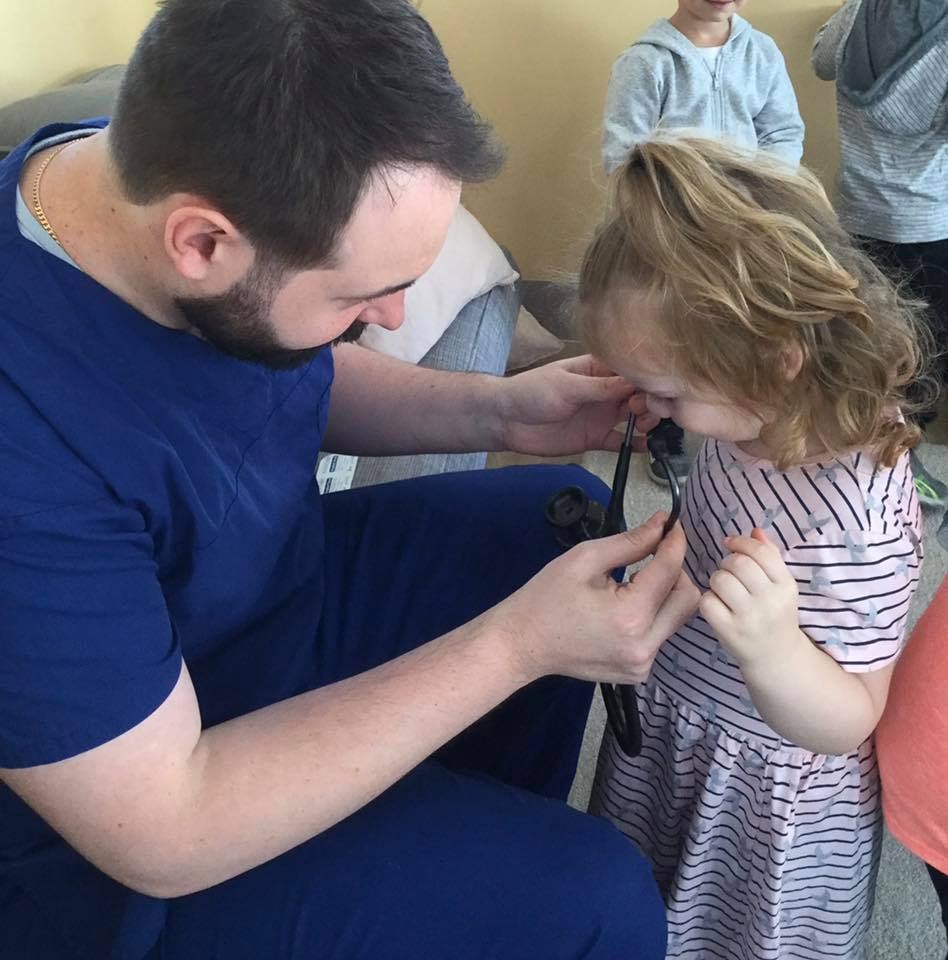 A visiting parent in scrubs showing a child how a stethoscope works