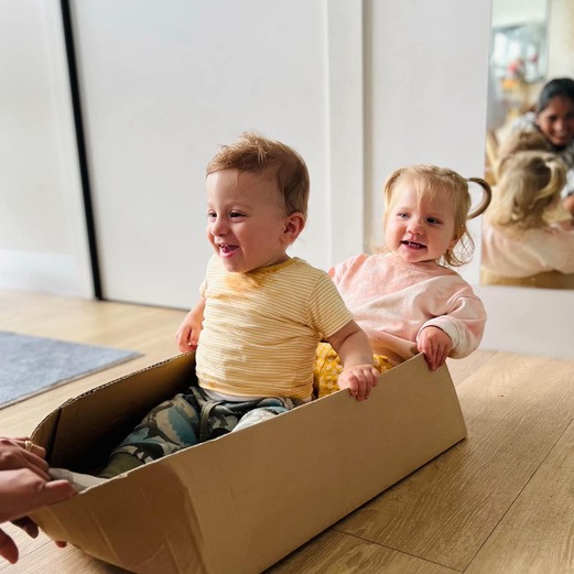 Two toddlers laughing in a cardboard box