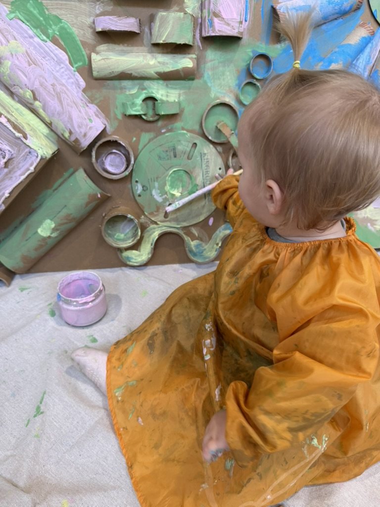 A baby painting a cardboard sculpture