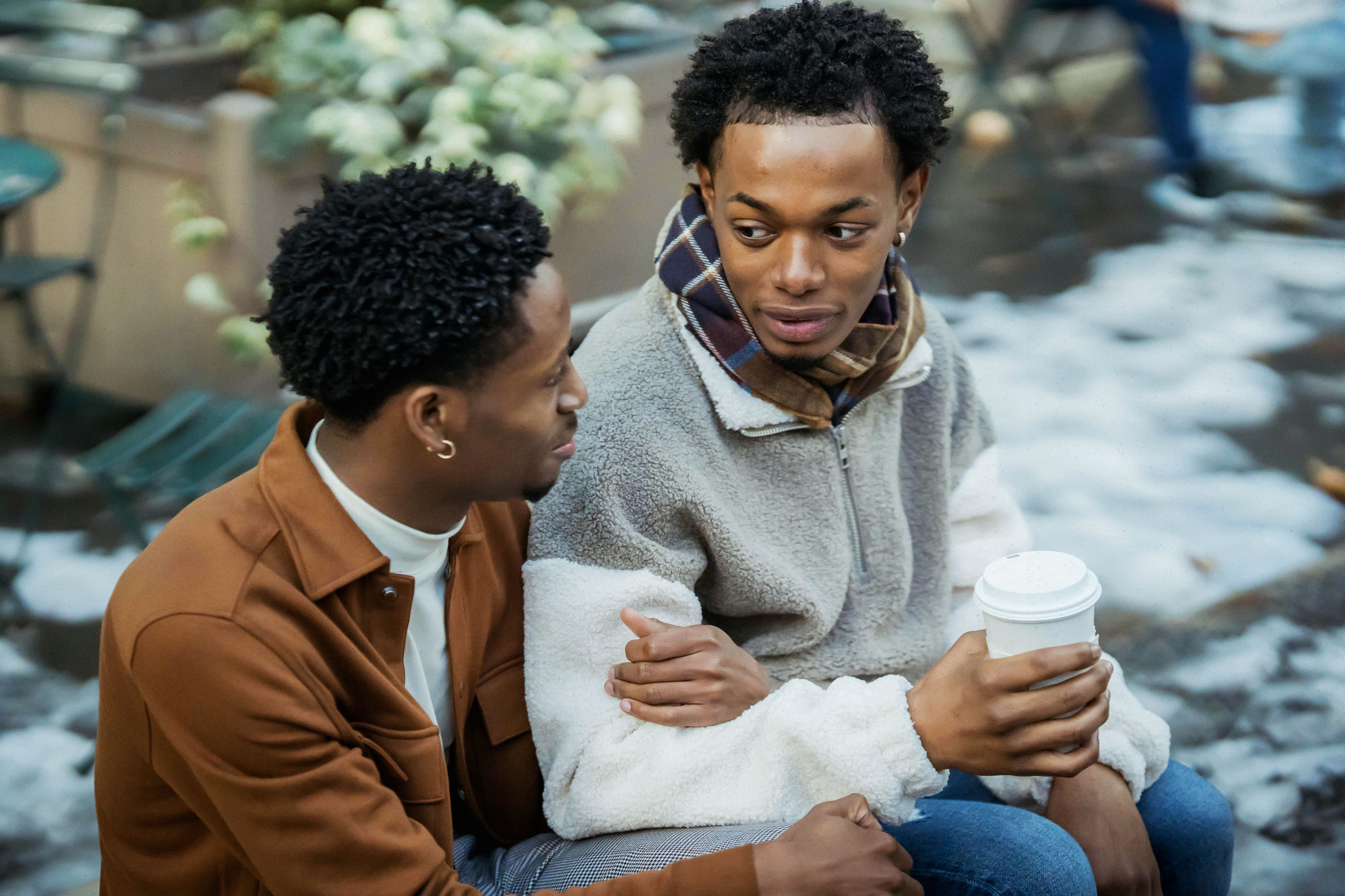 Two men sitting close together outdoors in winter, having a warm and caring conversation, illustrating emotional connection and intentional dating during cuffing season.