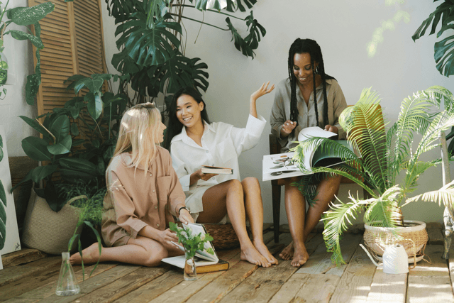  Three women relaxing and engaging in lively conversation surrounded by houseplants—demonstrating different communication styles through expressive body language, active listening, and connection.
