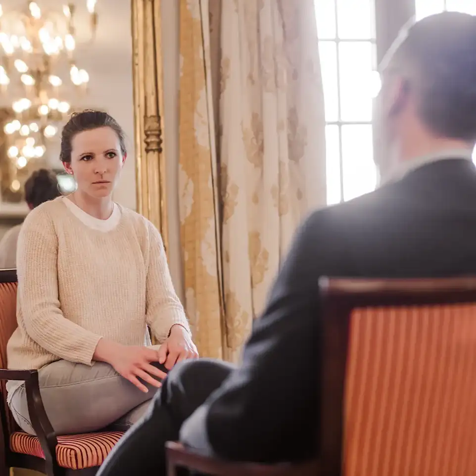 Eine Patientin in einer Therapiesitzung mit ihrem Therapeuten. Hinter ihr hängt ein Spiegel.