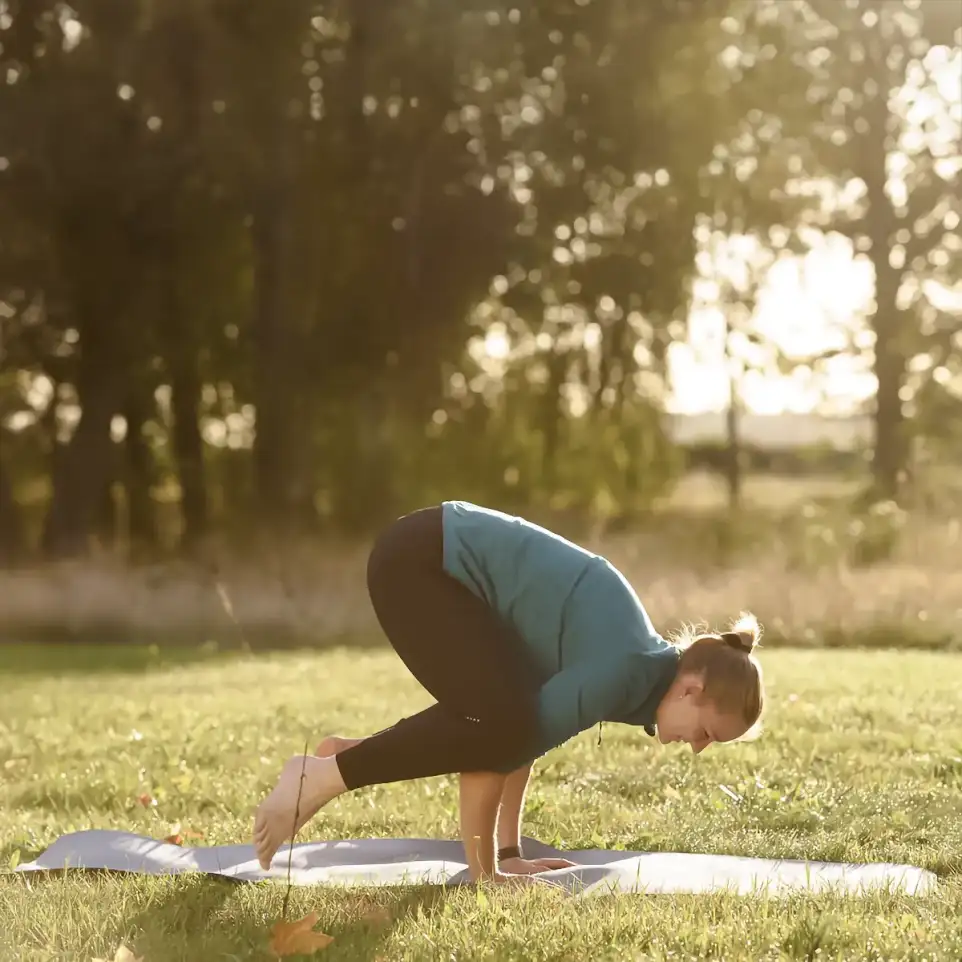 Eine Frau stützt sich auf ihre Hände in einer Yogaposition während ihre Füße leicht vom Boden abheben.