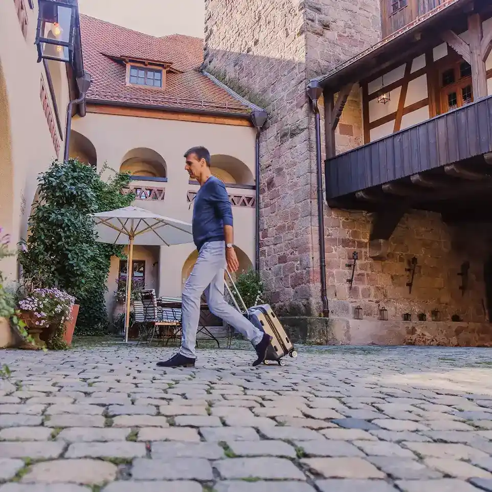 Ein Mann zieht einen Koffer hinter sich her und läuft auf den Eingang der Vincera Klinik Burg Wenberg zu.