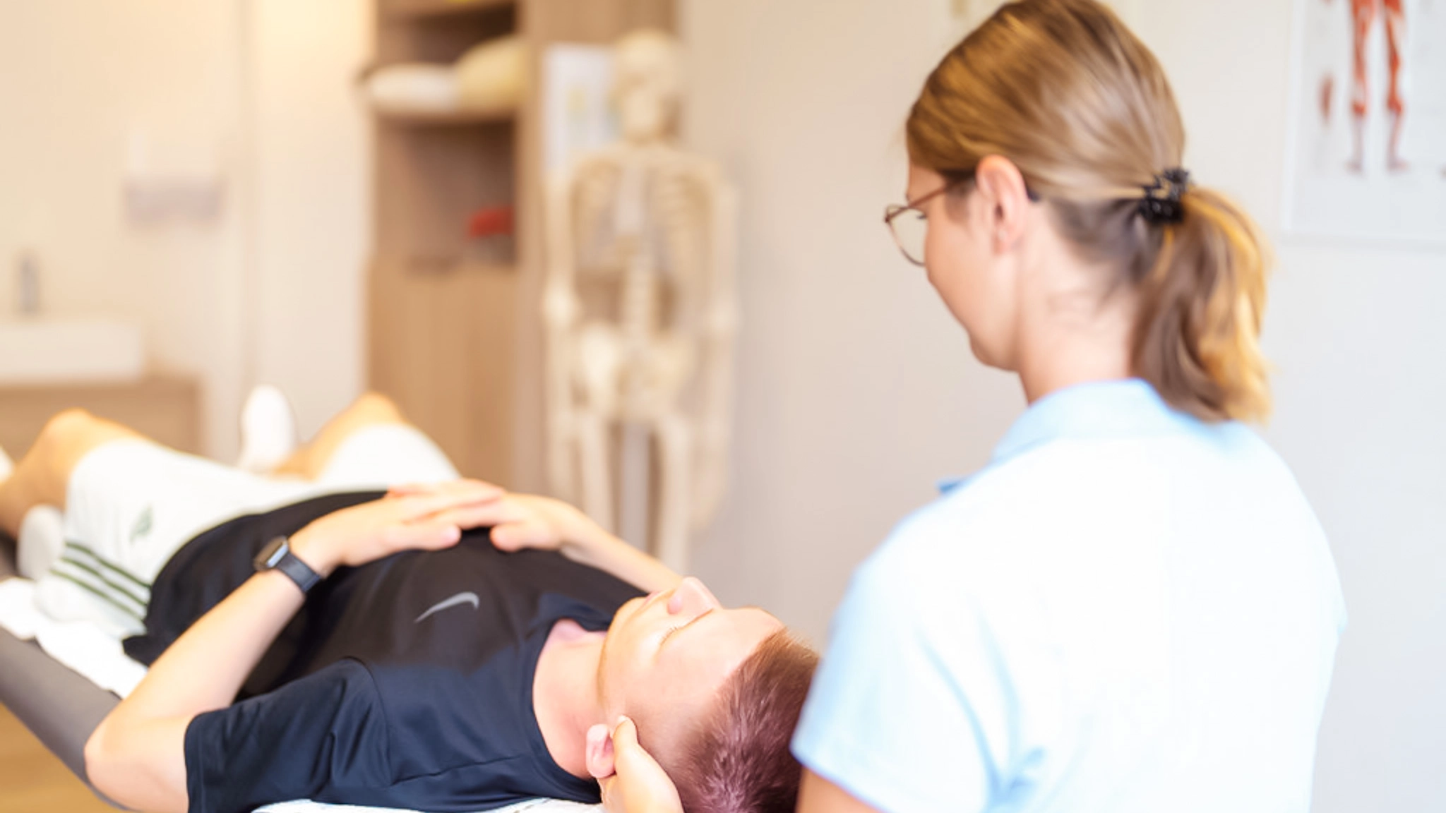 Eine Therapeutin führt eine medizinische Massage bei einem Mann durch, der auf dem Bauch liegt.