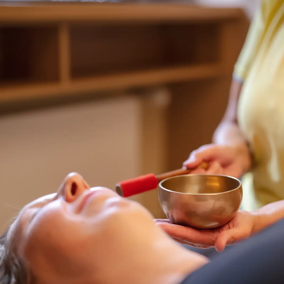 Eine Therapeutin hält eine Klangschale neben das Ohr einer Patientin.