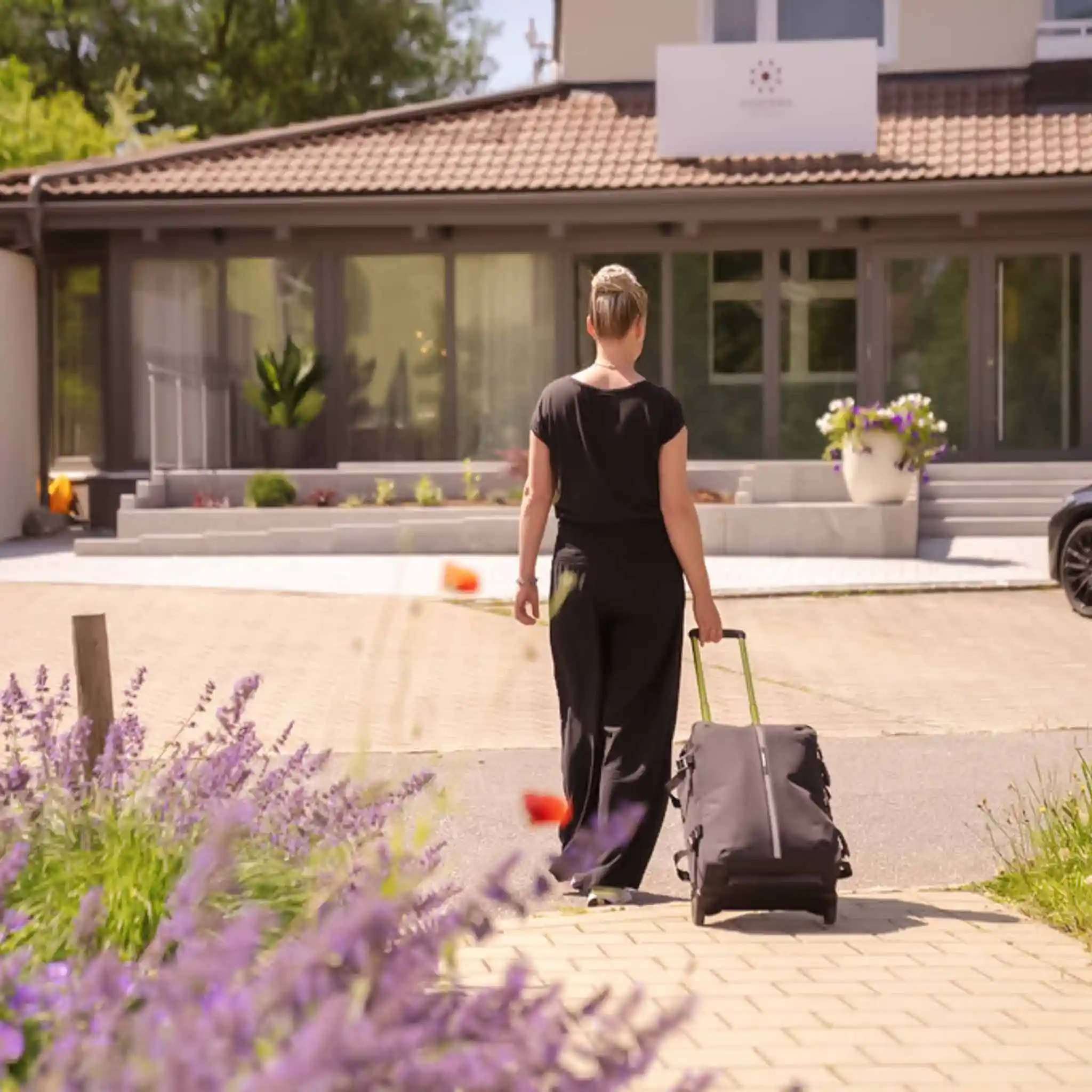 Eine Patientin bei der Anreise in einem Vincera Standort. Sie zieht ihren Koffer hinter sich her und läuft auf den Eingang zu.