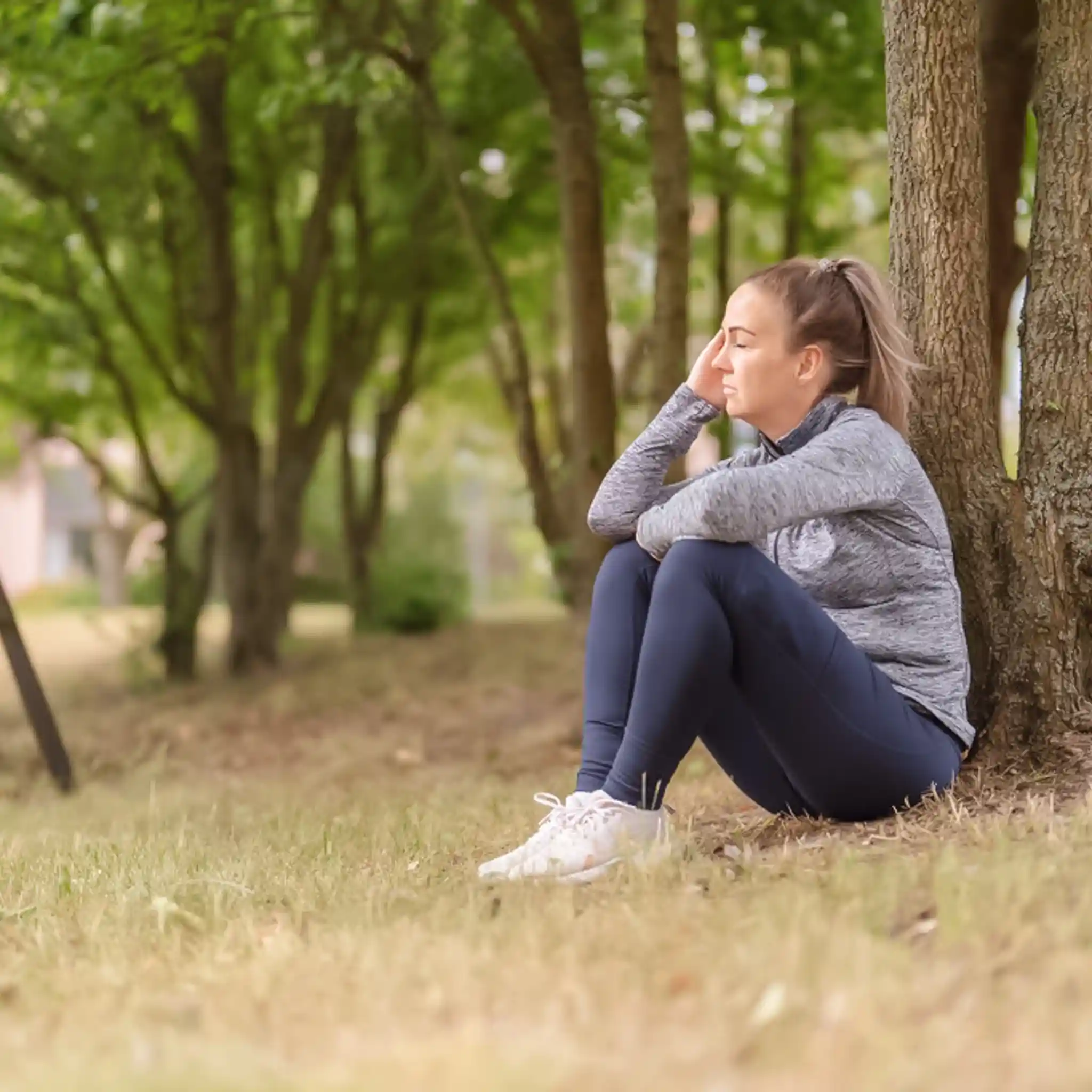 Eine Patientin sitzt an einen Baum gelehnt mit der Hand an ihrer Schläfe