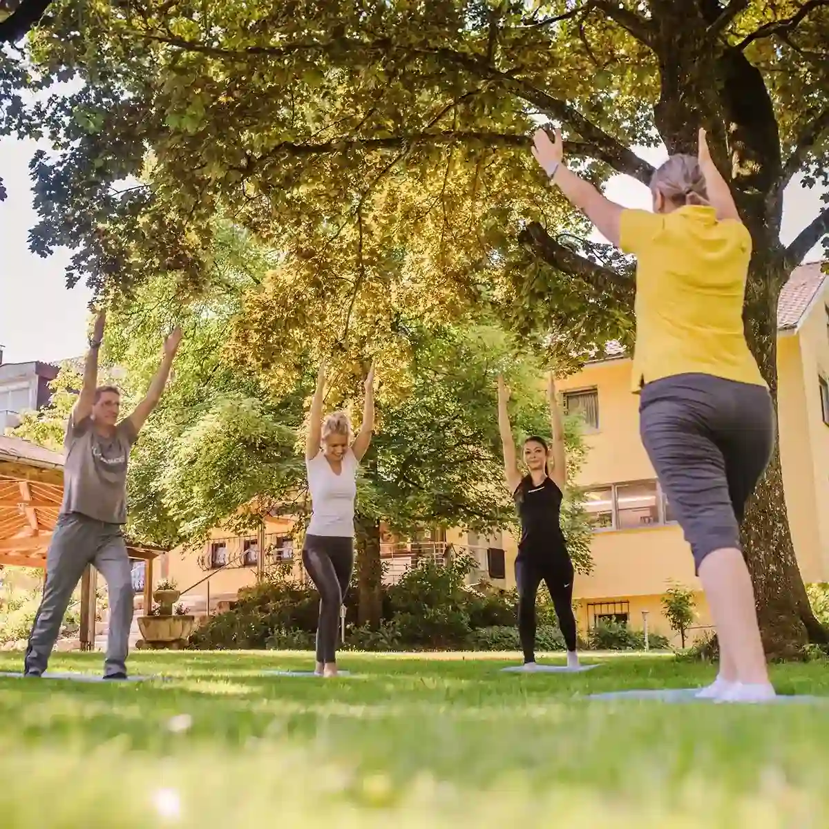 Eine Gruppe Patienten macht gemeinsam im Garten Yoga.