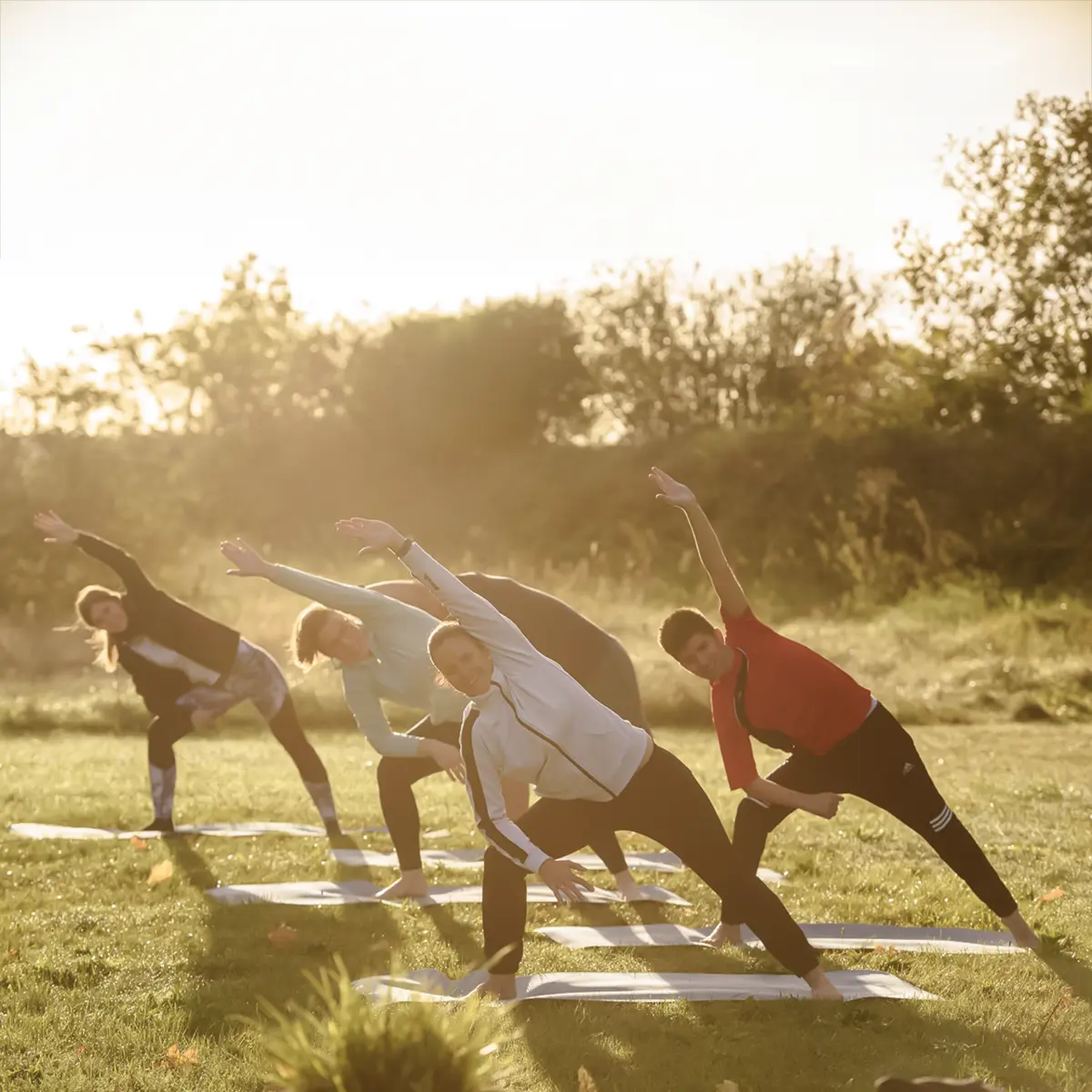 Eine Gruppe Patienten macht gemeinsam Yoga auf einer grünen Wiese.