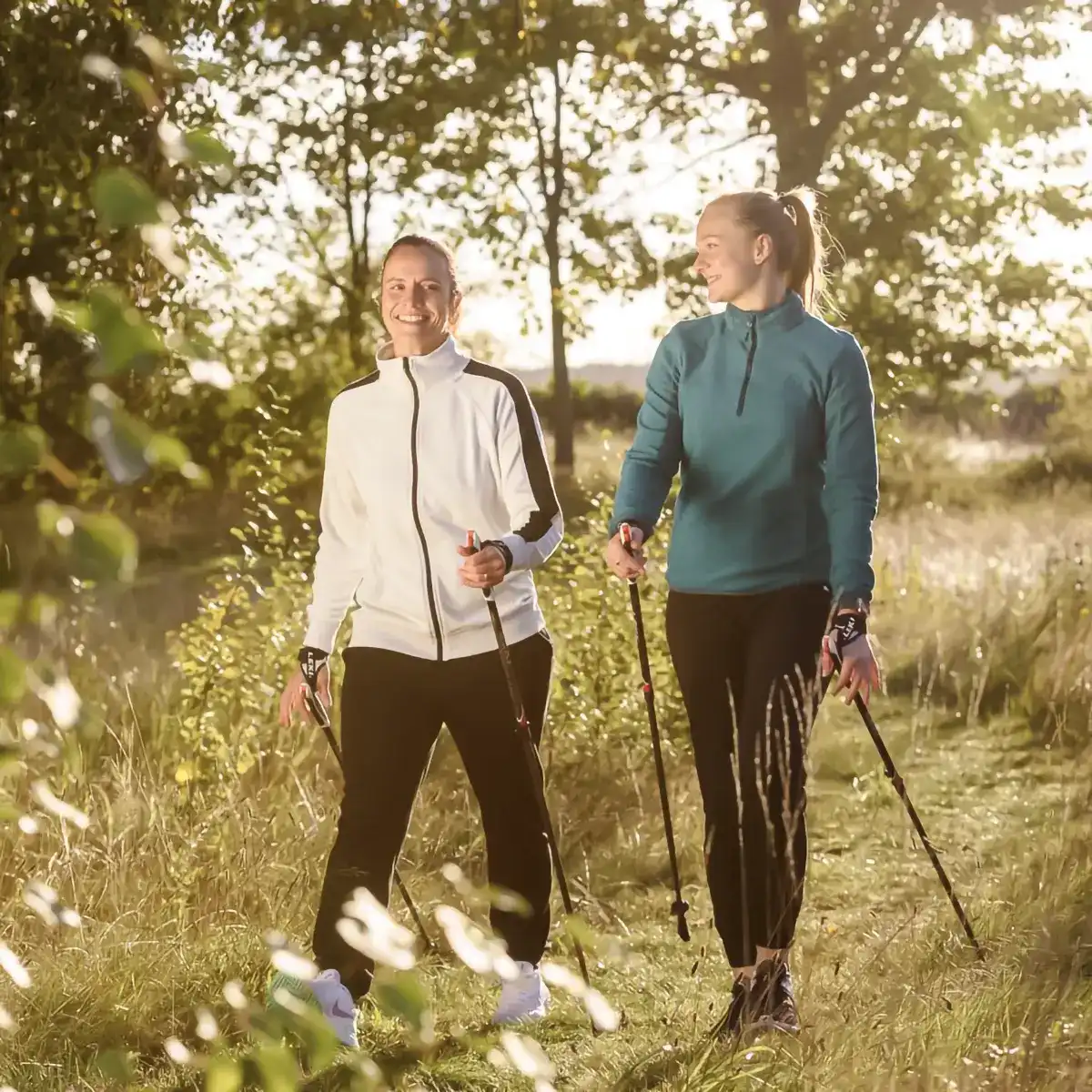 Zwei Patientinnen gehen lachend nebeneinander her beim Nordic Walking.
