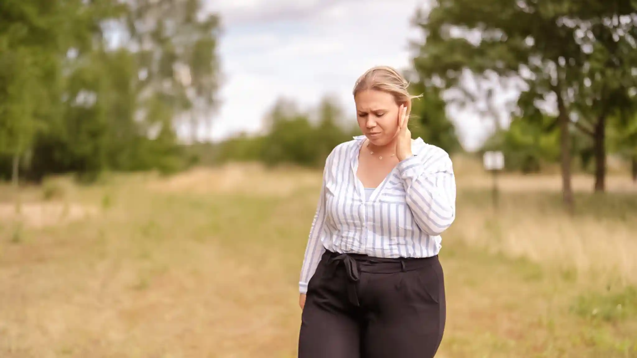 Eine Frau läuft auf einer Wiese und hält sich mit gequältem Blick das Ohr.