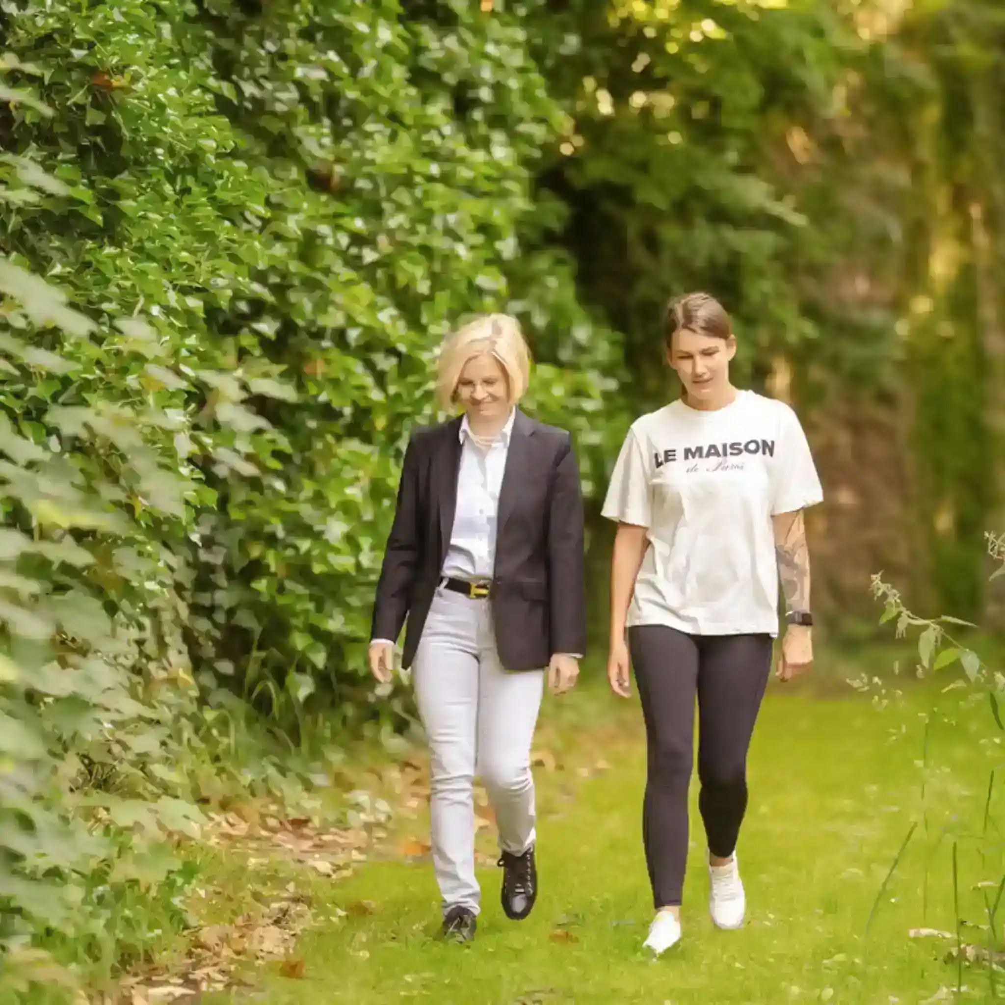 Patientin läuft neben Therapeutin durch den Garten 